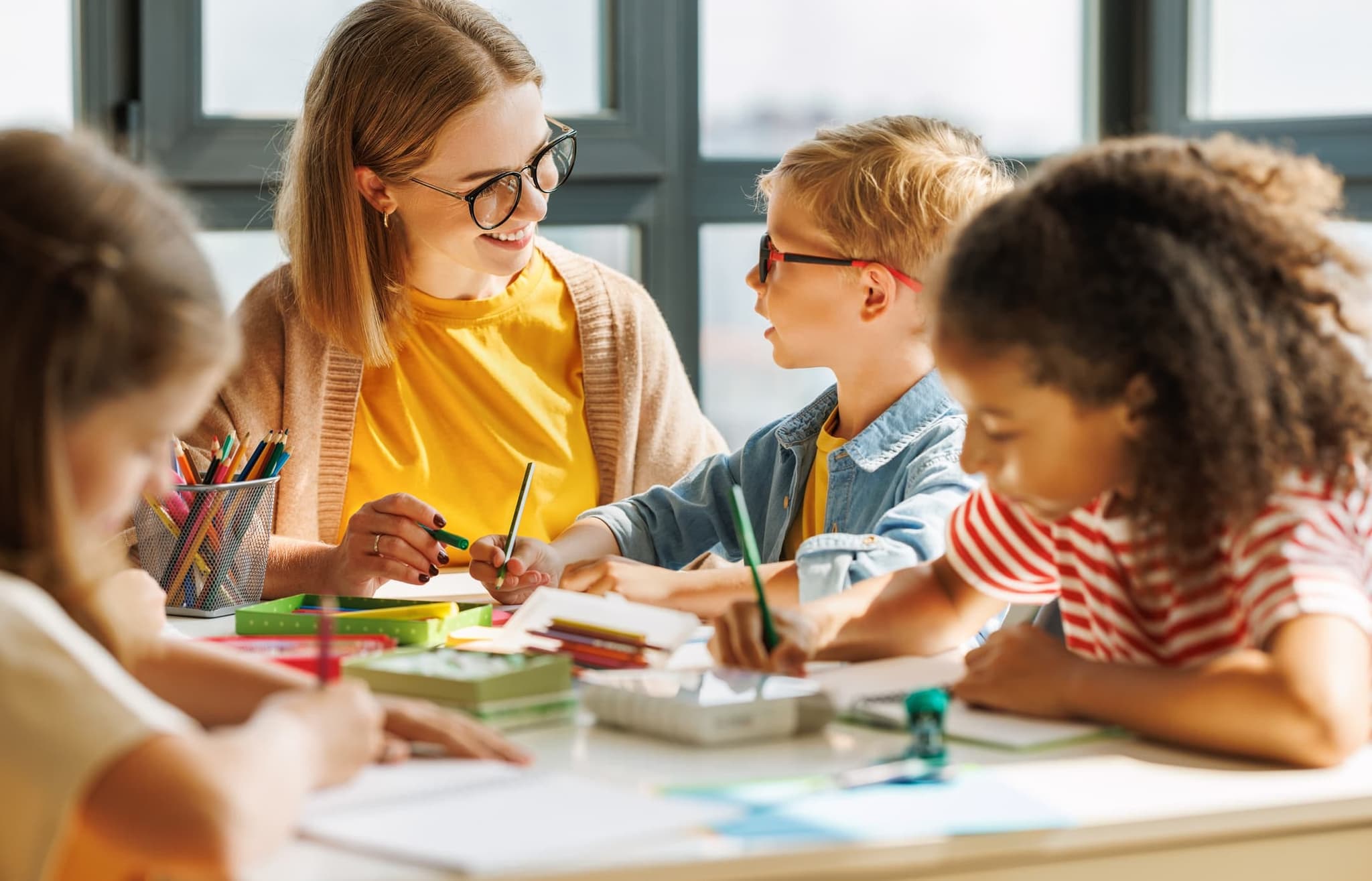 Teacher helping young students with a writing/craft activity at a classroom table